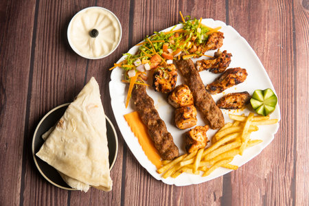 Turkish special mix grill with Chicken Tavuk, shish tawook, chicken kebab, ouzi chicken, Beef Adana, pita bread, hummus, and fries served in plate isolated on wooden table top view of turkish foodの写真素材