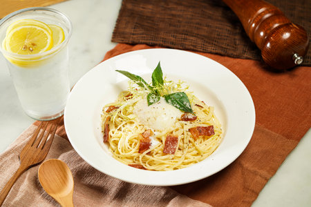 with lemonade, wooden spoon Linguine Carbonara with Soft Boiled Egg or Hot spring egg carbonara pasta and fork served in plate isolated on napkin and dining table side view of italian foodの写真素材