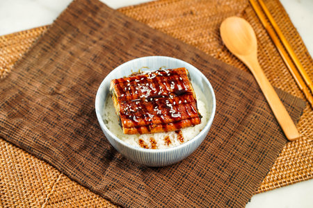 Teriyaki eel donburi with rice, chopsticks and spoon served in bowl isolated on napkin side view of Japanese foodの写真素材