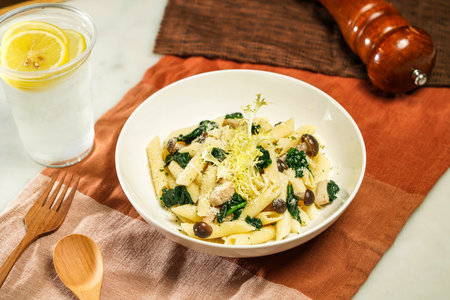 Penne with Spinach and Mushroom with wooden spoon and fork served in plate isolated on napkin and dining table side view of italian foodの写真素材