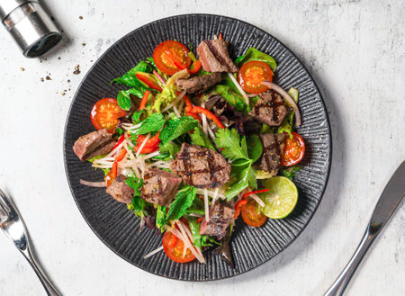 Wagyu Beef Thai Salad with cherry tomato, onion, lemon, mint and coriander served in plate isolated on background top viewの写真素材