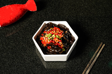 Spicy and sour fungus with red chilli pepper, sesame seeds and chopsticks served in dish on dark...