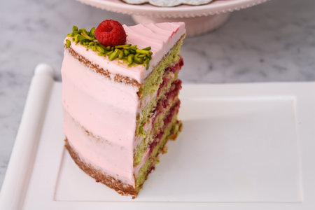 layered Raspberry Pistachio Cake slice frosted with light pink cream and garnished with raspberries and chopped pistachios side view of delicious dessertの写真素材