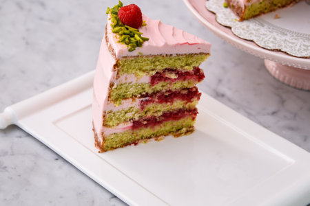 layered Raspberry Pistachio Cake slice frosted with light pink cream and garnished with fresh raspberries and chopped pistachios side view of delicious dessertの写真素材