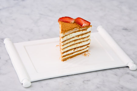 Slice of Classic Medovik Honey Layer Cake layers of honey sponge and creamy filling topped with strawberry slices served in tray isolated on grey background side view of classic dessertの写真素材