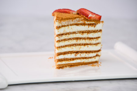 Slice of Classic Medovik Honey Layer Cake layers of honey sponge and creamy filling topped with strawberry slice served in tray isolated on grey background side view of classic dessertの写真素材