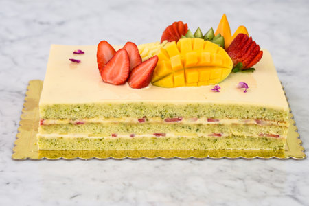Elegant Pistachio Layer Cake with Tropical Fruit including strawberries, mango, kiwi, and pineapple, along with delicate rose petals side view of flavorful dessertの写真素材
