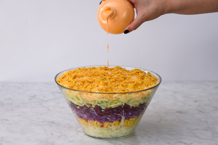 Fresh Seven Layer Salad in a clear glass bowl with layers of shredded lettuce, corn, red cabbage, green cabbage, dripping creamy sauce, and a crunchy crushed chips closeup side view of classic saladの写真素材