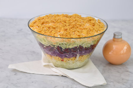 Seven Layer Salad in a clear glass bowl with shredded lettuce, corn, red cabbage, green cabbage, and crushed chips isolated on napkin side view of classic and colorful saladの写真素材