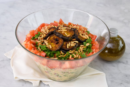 Mediterranean Couscous Salad with Grilled Eggplant on napkin featuring fluffy couscous, tomatoes, parsley, grilled eggplant slices, and toasted pine nuts with a olive oil bottle side viewの写真素材
