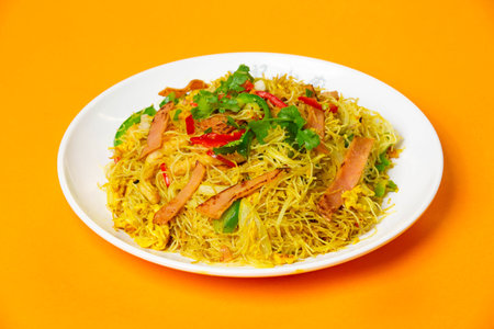 Singapore Fried Rice Noodles including rice vermicelli stir fried with ham, vegetables, cilantro and red chilies served in plate isolated on orange background side viewの写真素材