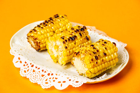 Grilled Corn on the Cob served in plate isolated on orange background side view