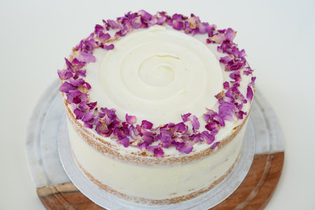 Rose Petal Cake with floral decor and rose petal garnish on decorative wooden stand closeup side...