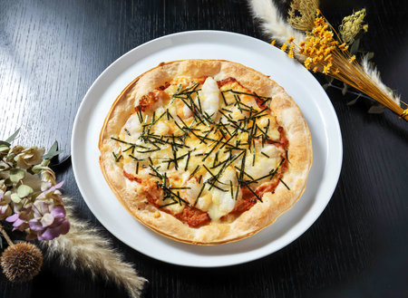 A delicious seafood pizza on a white plate surrounded by flowers on a dark wooden table, perfect for a culinary delightの写真素材