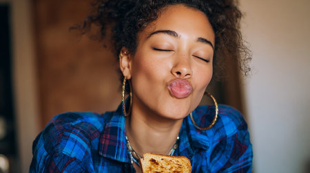 Young african american woman in the kitchen eating a piece of breadの素材