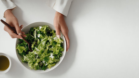 Top view of female hands holding bowl with fresh green salad on white backgroundの素材
