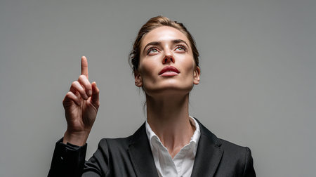 Portrait of a young business woman pointing up isolated on a gray backgroundの素材