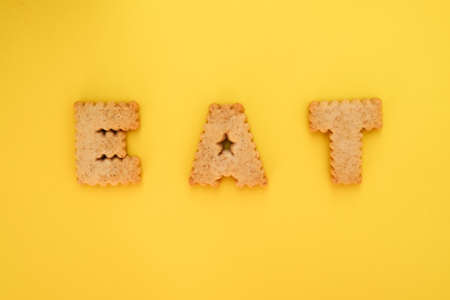 Cookie alphabet symbols E A T on top view with yellow backgroundの写真素材
