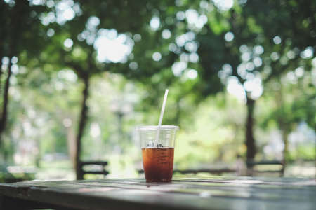 a plastic cup of iced americano (black coffee) on the wood plank table in the gardenの写真素材