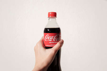 Bangkok , Thailand - JANUARY 18 ,2022 : Hand hold a bottle Coca-Cola on white background. Coca Cola...