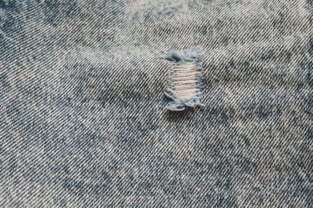 Hole and Threads on Denim Jeans. Ripped Destroyed Torn Blue jeans background. Close up blue jean texture.の写真素材