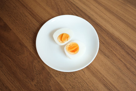 Sliced Boiled egg in white ceramic plate on wooden table.の写真素材