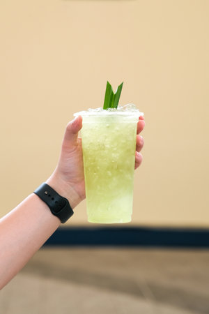 Ice pandan juice in plastic glass on woman hand and green pandan leaf, Fresh herbal Juice at street...
