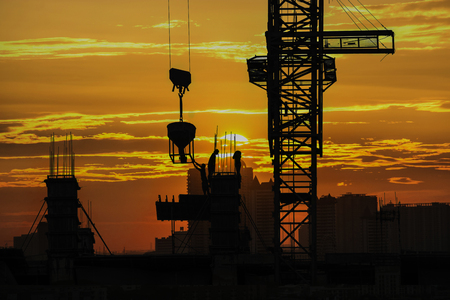 Silhouette of construction site & workers with sunset vibrant sky backgroundの写真素材