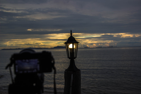 The camera is taking a picture of the sea, the lamp, the sunset at sunset.の写真素材