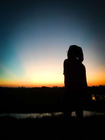 Shadow of Asian woman in Thailand standing to take photos of evening sunlight with smartphone, silhouette conceptの写真素材