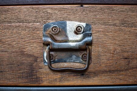 An old vintage handle installed on a dark brown wooden drawerの写真素材
