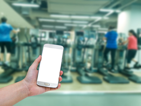 hand holding mobile smart phone with blur fitness gym equipment background,Vintage filterの写真素材