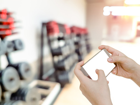 hand holding mobile smart phone with blur fitness gym equipment backgroundの写真素材