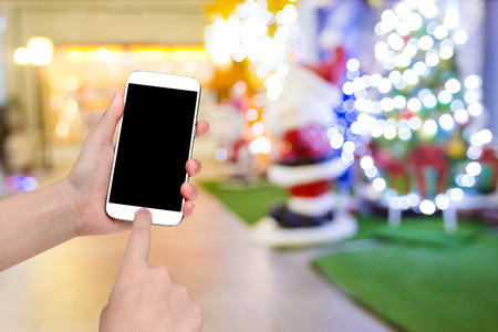 hand holding mobile smart phone with santa claus doll christmas blur backgroundの写真素材
