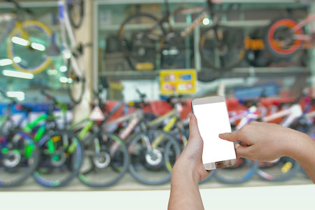 hand holding mobile smart phone with blurry showroom bicycle backgroundの写真素材