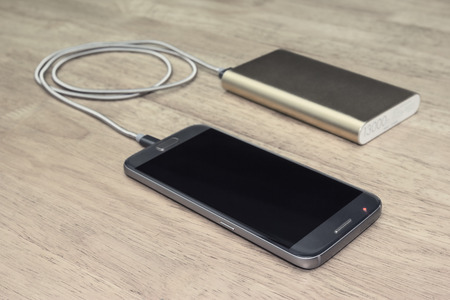 Smartphone charging with power bank on wood background,filter effect