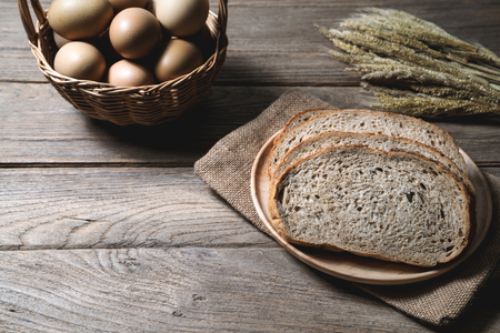 bread loaf and wheat ears and sack on wooden background.