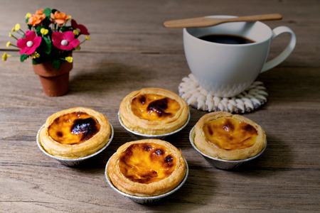 coffee with egg tart in aluminum foil cup on wood table