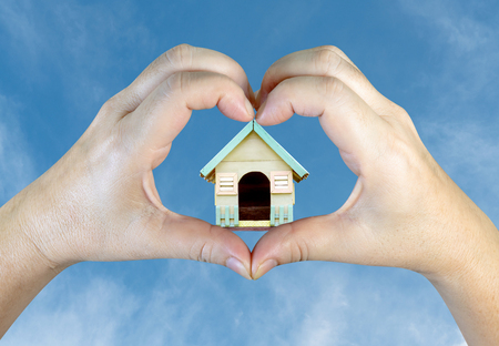 person hands making a heart shape with wooden house on sky backgroundの写真素材