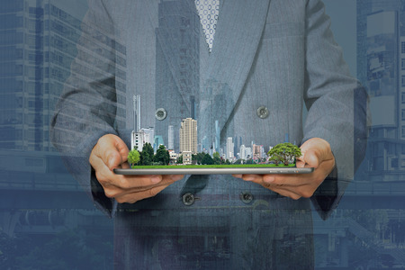 Double exposure with businessman holding tablet and city model in handsの写真素材