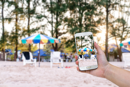 hand holding mobile smart phone with blur beach chair at coast background