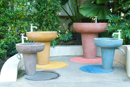 Colorful outdoor hand washing station with four terrazzo pedestal sinks of different heights in a...
