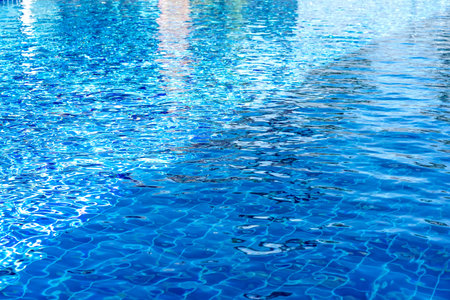 Clear blue swimming pool water with sunlight reflections and ripples. The tiled bottom is visible...