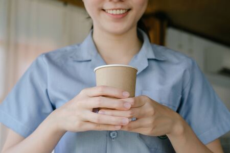 Hot drink in a craft plastic cup with a white cap in the hands of a young girl with a red manicure...