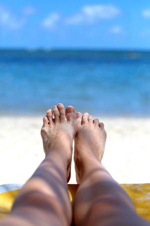 girls feet in the sand on the background of the oceanの写真素材
