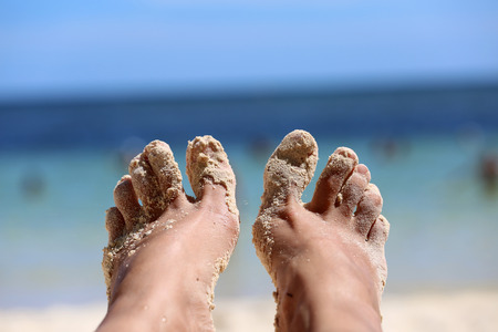 girls feet in the sand on the background of the oceanの写真素材