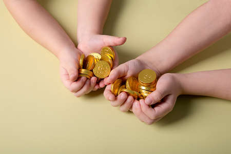 Children's hands hold gold coins on a yellow background.の写真素材