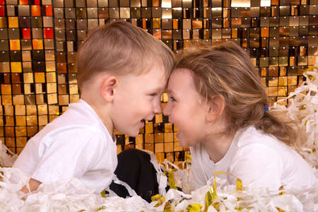A boy and a girl play in a pile of cut white and gold paperの写真素材