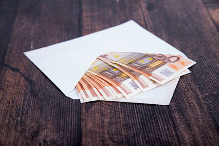 Euro, in denominations of fifty, in a white open envelope on a dark wooden backgroundの写真素材