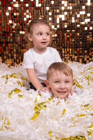 A boy and a girl play in a pile of cut white and gold paperの写真素材